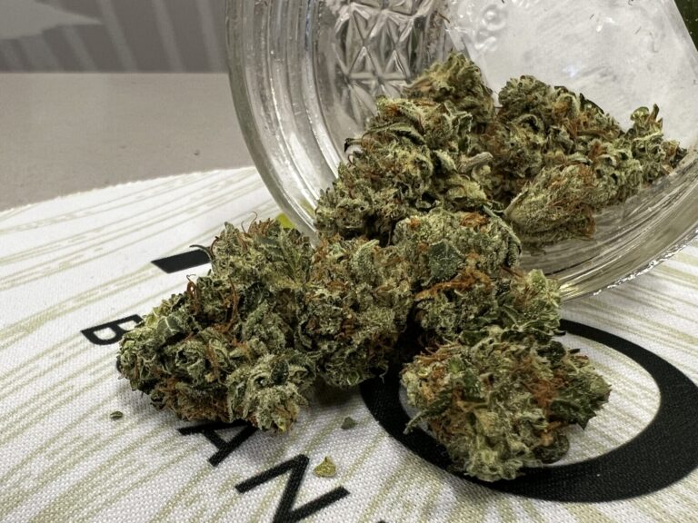 A glass jar with marijuana in it sits on top of a table.
