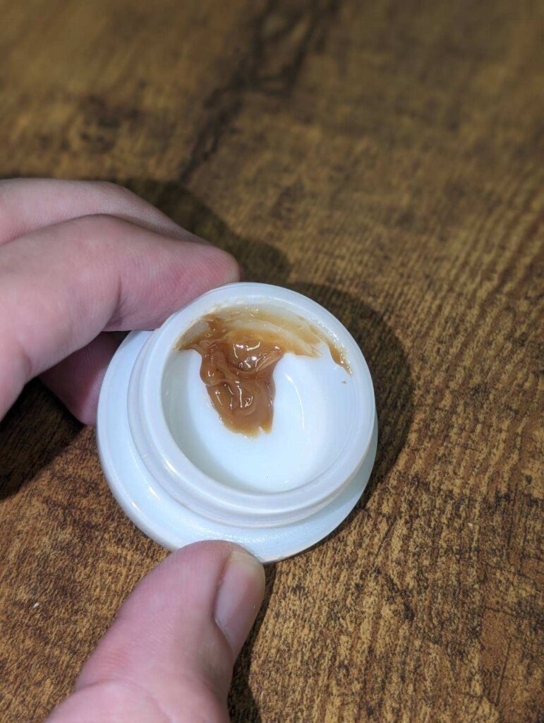 A person holding a small container with a brown liquid in it, showcasing the Purple Liliko'i Strain.