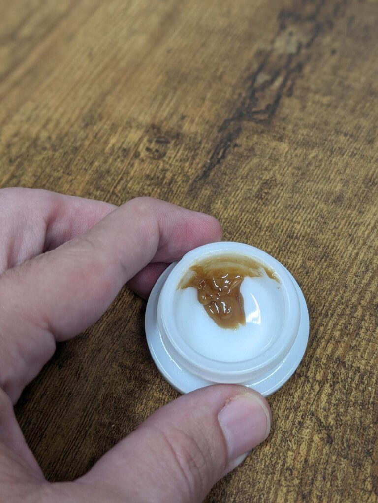 A person holding a small piece of chocolate on a table, infused with the exotic Purple Liliko'i strain.