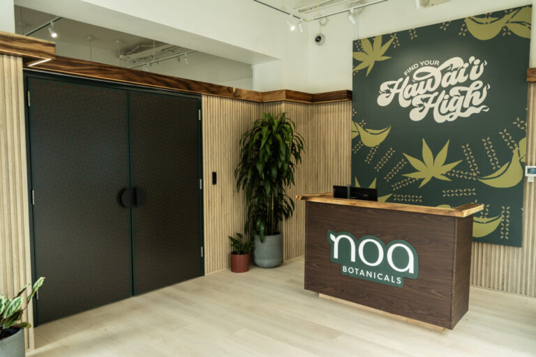 Reception area of Noa Botanicals’ Waikiki cannabis dispensary, featuring locally crafted wood design, lush greenery, and a mural reading 'Find Your Hawai‘i High' — a welcoming and modern space for cannabis in Waikiki