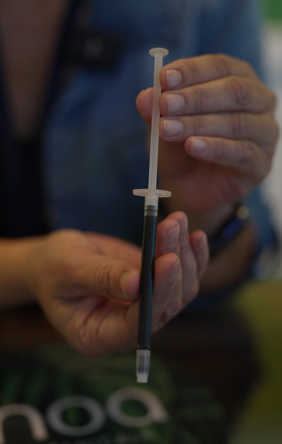 A person holds a syringe filled with a dark liquid, reminiscent of Cannabis Rick Simpson Oil, set against a blurred background.