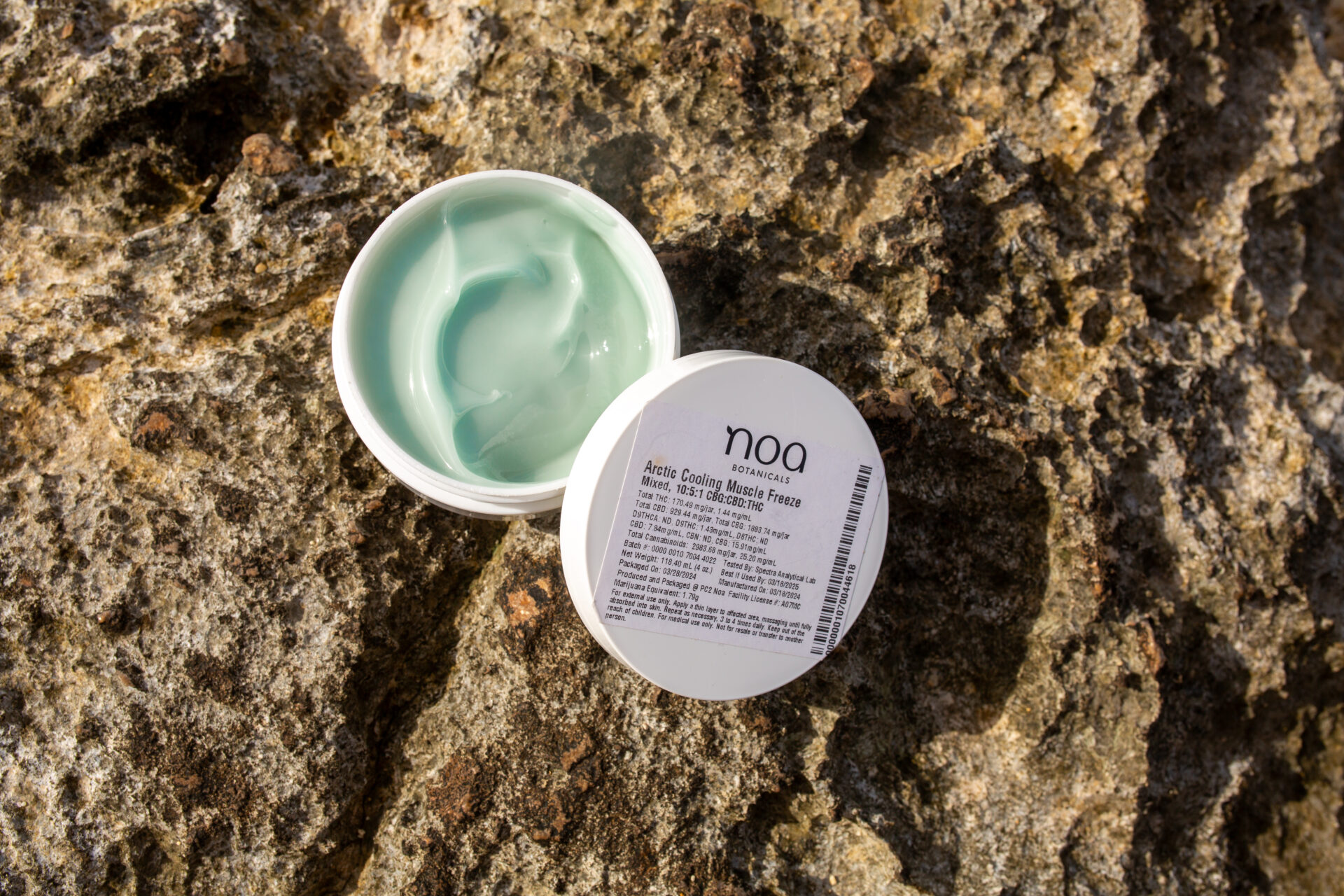 An open container of noa Arctic Cooling Intensive Freeze Mask sits on a textured rock surface, showing light green gel inside, inspired by the soothing properties of medical cannabis.